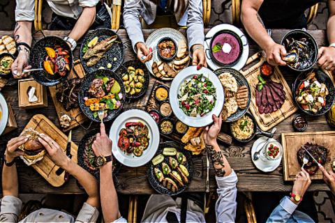 Photo of food on table with people selecting plates to eat